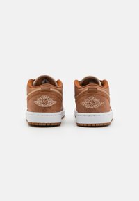 Une paire de sneakers Air Jordan en daim brun vue de l'arrière, montrant des semelles intermédiaires blanches et un logo d'ailes en relief sur les talons.