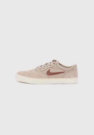 Basket basse en daim beige avec logo Nike Swoosh marron, semelle en caoutchouc blanche et laçage à l'avant, présentée sur un fond clair uni.