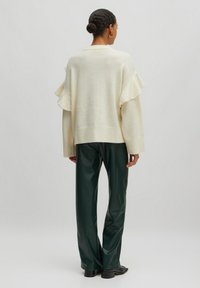 Crème kleurige trui met volants op de mouwen, losse pasvorm en geribbelde zoom, gecombineerd met high-waisted donkergroene nep leren broek.