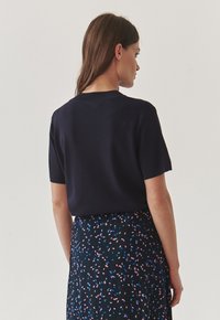 Marineblauw kortmouwen top van een zachte stof, gecombineerd met een gebloemde rok met roze en blauwe accenten op een zwarte achtergrond.