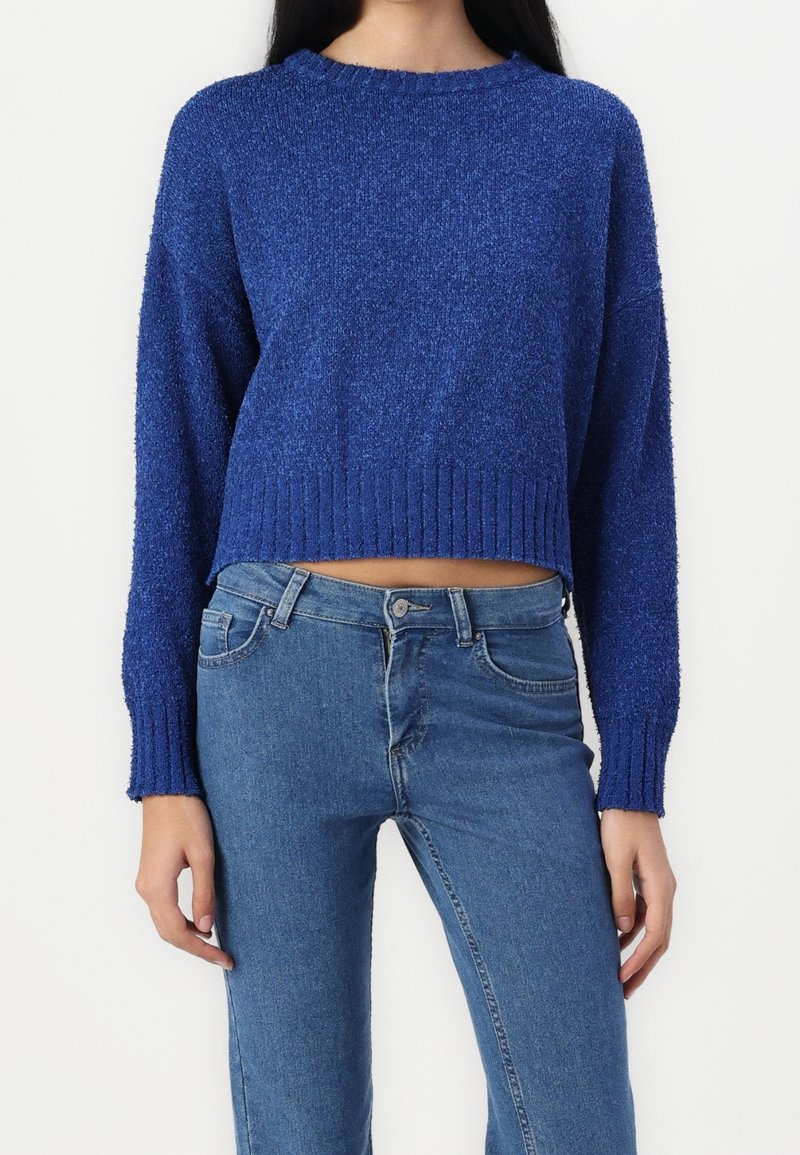 Pull bleu en tricot avec une finition texturée, ourlet côtelé et manches longues. Associé à un jean en denim bleu clair.