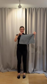 Vrouw staat voor lichte gordijnen en houdt een zwart-wit geruit doek vierkant met beide handen vast.