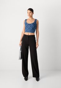Top de mezclilla azul recortado con un patr�ón geométrico, combinado con pantalones de tiro alto de pierna ancha negros y elegantes tacones negros puntiagudos. Bolso de mano plateado.