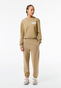 Brun sweatshirt och matchande joggers i mjukt tyg; har ribbade ärmslut, resårmidja och en grafisk detalj på bröstet.