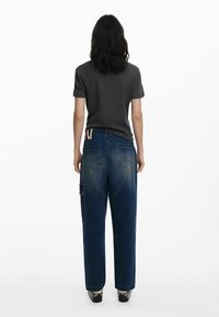 Camiseta gris oscuro combinada con jeans de denim azul de corte holgado. Los jeans tienen bolsillos traseros y un bolsillo cargo lateral. El calzado tiene un patrón texturizado.