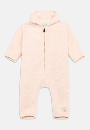 Salopetă roz deschis din fleece, cu fermoar în față, mâneci scurte și guler înalt. Are o textură moale și o etichetă mică cu brandul pe picior.