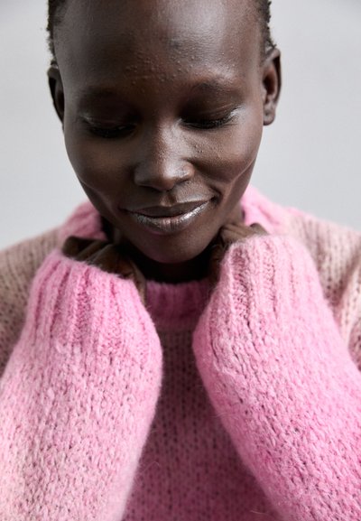 Maglione rosa a maglia con una finitura texture e morbida. Le maniche lunghe presentano polsini a coste, indossato vicino al collo, evidenziando un design accogliente.