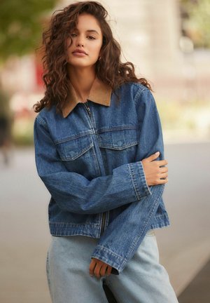Denim jakker, millel on kaelusest puuvillasest kootud krae, ees lukk ja kaks rinnataskut. Omab laiu varrukaid ja vabamat istuvust. Helesinine värv.