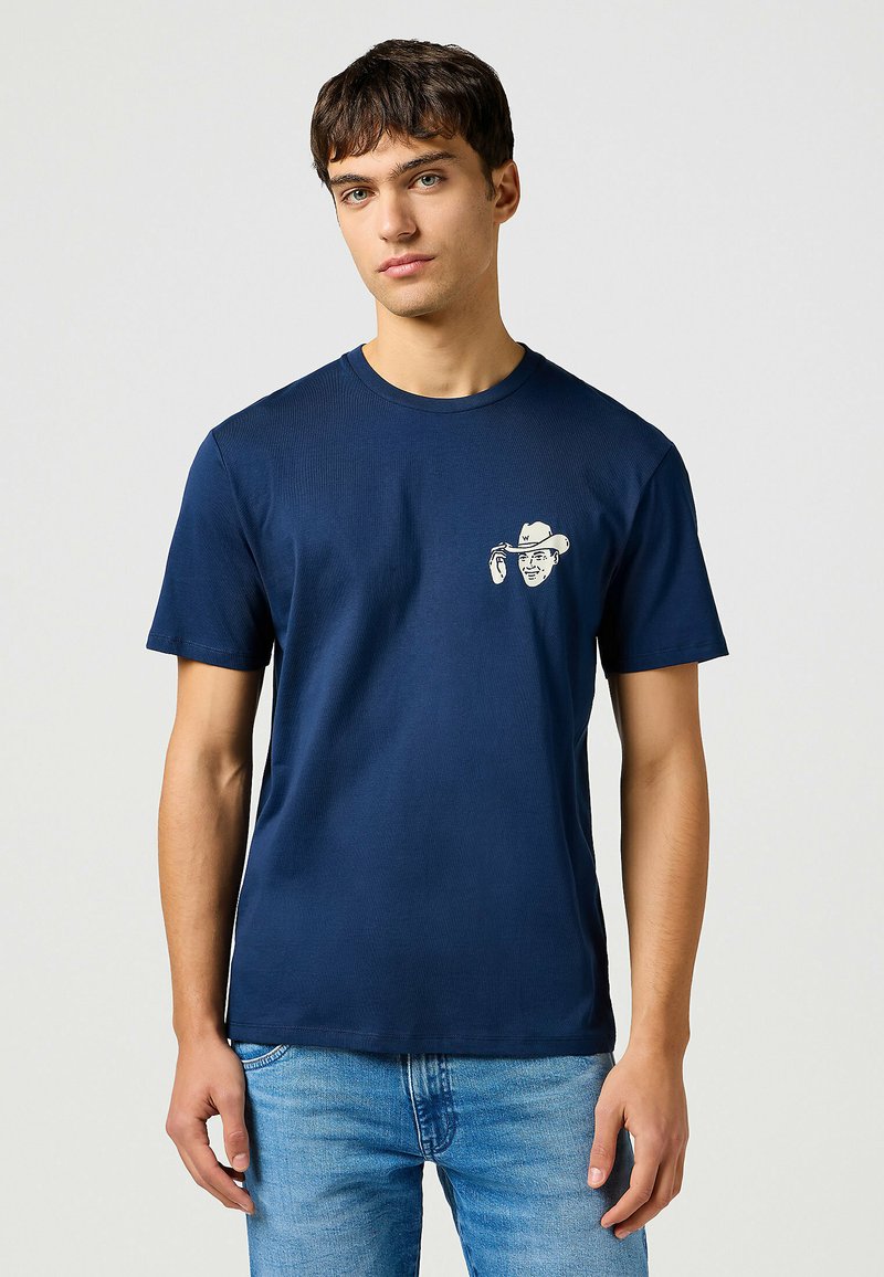 Camiseta de algodón azul marino de manga corta, con un gráfico blanco de un sombrero de vaquero y una cara en el área del pecho izquierdo.