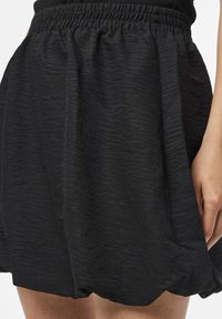 Černá plisovaná sukně s elastickým pasem, vyrobená z texturované látky, s mírně rozšířeným tvarem a jemnými detaily na povrchu.