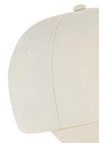 Beżowa czapka z zaokrągloną koroną, gładką fakturą i kontrastującymi białymi szwami; ma guzik u góry i wygięty daszek.