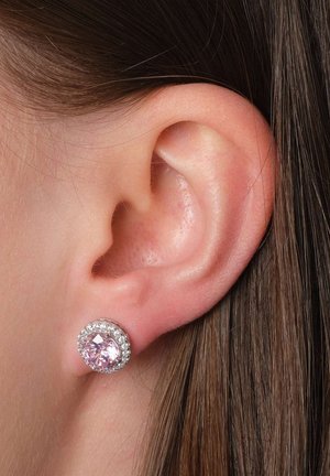 Ohrringe mit einem pinken Edelstein in der Mitte, umgeben von kleinen klaren Kristallen. Die Metallfassung ist aus Silber. Nahaufnahme eines Ohres.