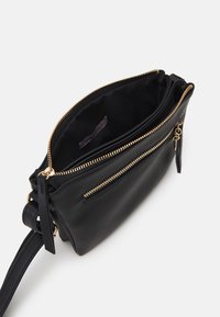 Sac bandoulière en cuir noir avec un compartiment principal zippé et une poche extérieure zippée. Quincaillerie en ton doré et doublure en tissu.