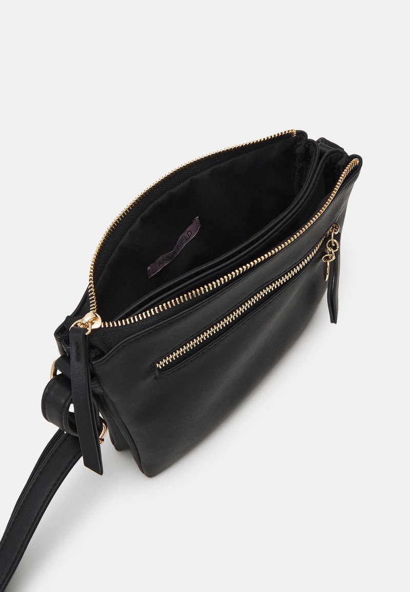 Bolso cruzado de cuero negro con un compartimento principal con cremallera y un bolsillo exterior con cremallera. Herrajes en tono dorado y forro de tela.