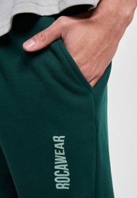 Grønne bomulds-joggers med sidelommer og et logo-print med teksten "ROCAWEAR" i lys farve. Taljen er elastisk for komfort.