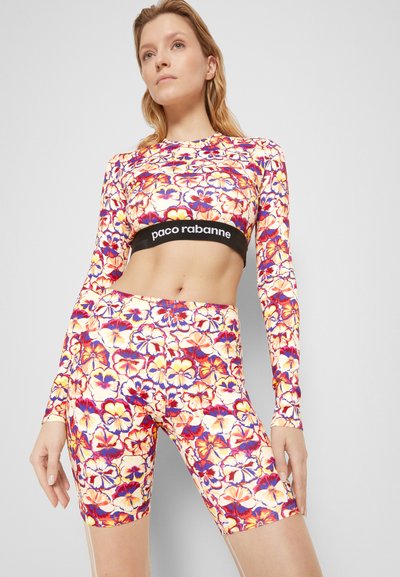 Conjunto de roupa ativa com padrão floral, composto por mangas longas e calções. O tecido apresenta cores vibrantes: laranja, roxo e creme. Cintura elástica preta com marca.