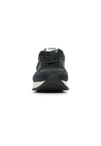 Zwarte sportschoen van suède en mesh materialen, met een witte zool, afgeronde vorm en platte veters. Merkenlogo zichtbaar op de tong.