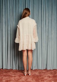 Šaty s bodkami z ľahkej látky s volánikovými rukávmi a vrstvenou sukňou, zdobené malými farebnými bodkami na krémovom pozadí.