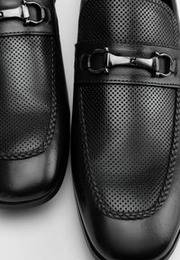 Zapatos de cuero negro con detalles perforados y una textura suave. Presentan una hebilla decorativa en el empeine. Forma de punta redonda.