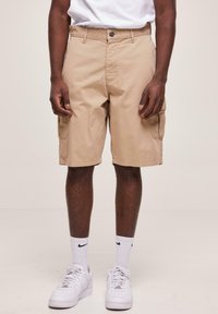 Shorts cargo khaki avec poches latérales, en coton, offrant une coupe décontractée et un design à jambe droite, associés à des baskets blanches et des chaussettes.