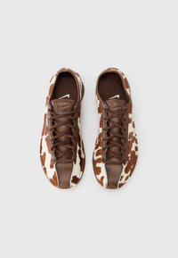 Pruunide ja valgete lehmakujuliste mustriga tossud, millel on sile nahast varbakate ja tugevad pruunid paelad. Keelel on logo ja tekstuuriga muster.