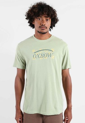 T-shirt à manches courtes vert clair en tissu doux, présentant un graphique central "OXBOW" avec des accents jaunes et une coupe décontractée.