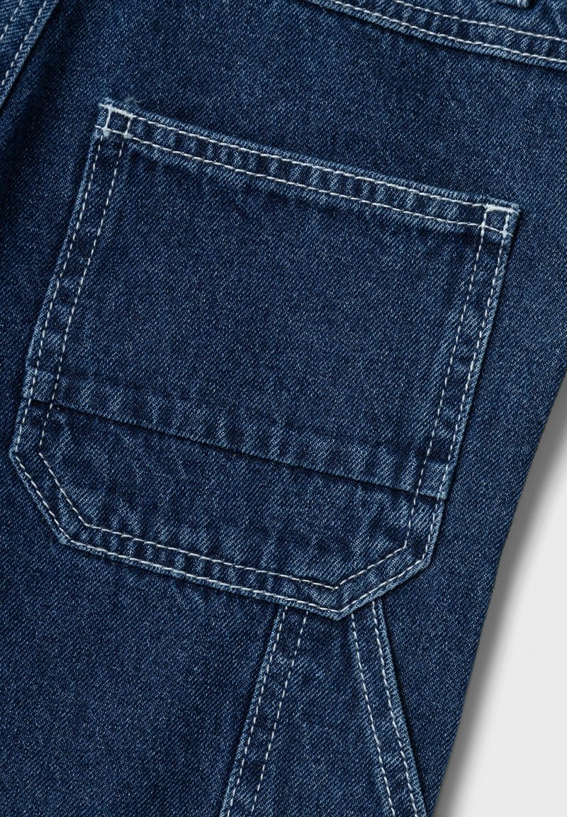 Close-up van denimstof met een rechthoekige zak en witte stiknaden. Het materiaal is donkerblauw, met een lichte textuur en duurzaamheid.