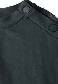 Mörkgrå bomulls-t-shirt med rund hals, utrustad med två stora, runda tryckknappar på ena axeln och ett slätt, strukturerat tyg.