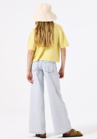 Suéter de punto de manga corta en un amarillo claro, combinado con jeans de pierna ancha en un azul claro. Un sombrero tipo bucket beige, sandalias marrones con dobles hebillas.