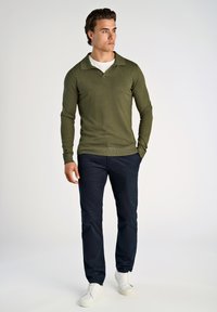 Olivgrüner Strickpullover mit kragenförmigem Ausschnitt, kombiniert mit marineblauen Hosen und weißen Sneakers. Texturiertes Material, slim fit Design.