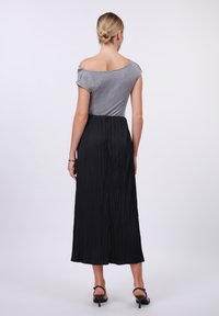 Top grigio off-the-shoulder abbinato a una maxi gonna nera con texture. La gonna presenta un design plissettato e una vita elastica.