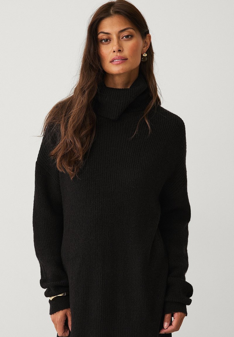 Sort strikket sweater med høj, foldet turtle neck og lange ærmer. Har et struktureret mønster og en tætsiddende silhuet.