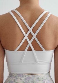 Witte sportbeha met gekruiste banden op de rug, gemaakt van gladde stof. De onderste zoom heeft een subtiele elastische band voor ondersteuning.