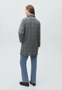 Gray checkered coat with a classic collar, long sleeves, and a relaxed fit, paired with light blue jeans and black boots.