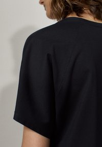 Czarny t-shirt z krótkim rękawem o luźnym kroju, wykonany z miękkiej bawełny. Posiada prosty okrągły dekolt i gładką fakturę.