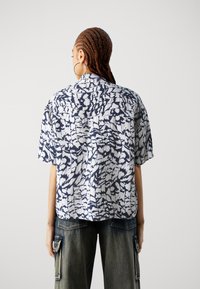 Maglietta a maniche corte con un motivo astratto blu navy e bianco, caratterizzata da un colletto con bottoni e un design comodo.