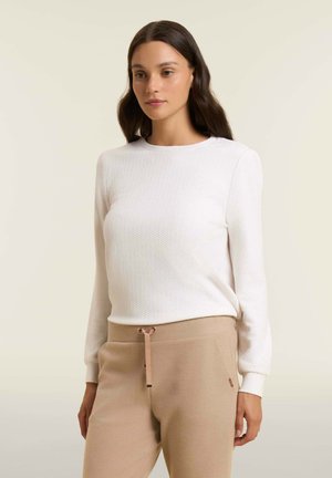 Top blanco de manga larga con textura y escote redondo, combinado con pantalones beige con cordón, mostrado sobre un fondo neutro.