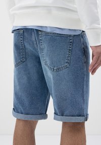 Shorts en denim bleu clair, avec des ourlets retroussés. Dispose de deux poches arrière, d'une couture discrète et d'une texture légèrement usée.