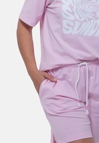 T-shirt di cotone rosa con una grafica a spirale bianca, abbinata a pantaloni corti rosa coordinati con vita regolabile e tasche laterali.