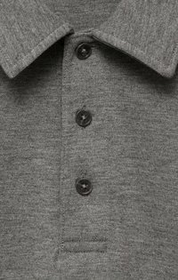 Grå polo skjorta med en texturerad stickad tyg, en platt krage och tre svarta knappar längs placket. Liten broderad fickdetalj ingår.