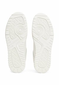 Semelles de baskets blanches en matériau en caoutchouc texturé. Présente des motifs circulaires et des rainures pour l'adhérence, avec un logo visible sur une semelle.
