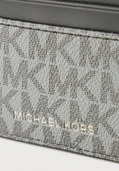 Gros plan sur un cuir texturé gris Michael Kors avec un motif répétitif "MK" et le nom de la marque embossé en argent.