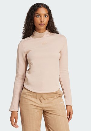 Lichtroze lange mouw shirt met een hoge kraag en subtiele logo op de borst, gecombineerd met tan gestreepte broek.
