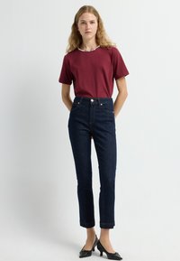 Burgundská košile s krátkým rukávem a korálkovým výstřihem, v kombinaci s tmavě modrými vysokými džínami a černými lodičkami se špičatou špičkou.