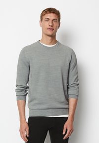 Grauer Strickpullover mit runder Halslinie und langen Ärmeln, der ein strukturiertes Muster sowie gerippte Bündchen und Saum aufweist, über einem weißen Hemd getragen.