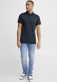 Polo shirt texturé bleu marine avec un col noir, associé à un jeans bleu clair et des baskets blanches avec des accents marine. Coupe décontractée.