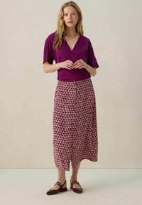 Un haut enveloppant violet associé à une jupe maxi à motif floral en violet et crème. Porté avec des chaussures plates marron. Design simple et coupe fluide.