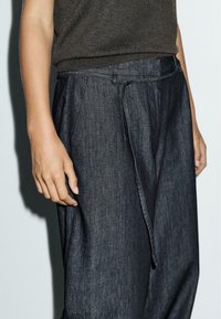 Donkerdenim broek met een losse pasvorm, voorzien van een platte voorkant, zichtbare stiksels en een gestrikte koord in de taille.