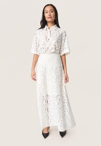 Weißes Spitze-Zweiteiler-Outfit mit einem kurzärmeligen Oberteil mit Kragen und einem langen, fließenden Rock mit floralem Muster und transparenter Textur.