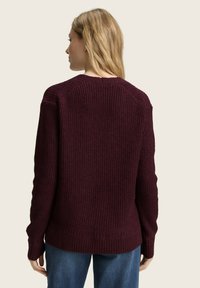 Pull en tricot bourgogne avec un design de côtes texturé, des manches longues et un col rond. Il présente une coupe légèrement ample et un ourlet en côtes.